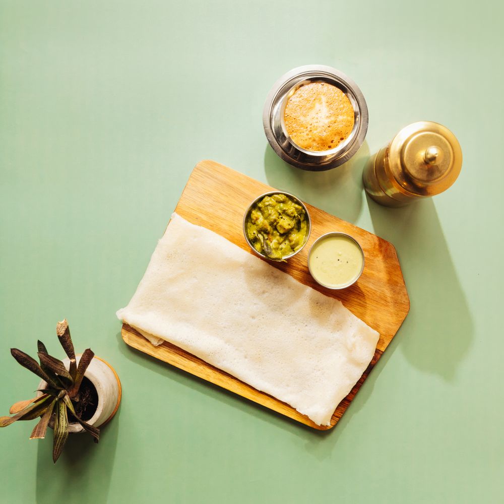 Neer dosa on a wooden board with coconut chutney and filter coffee