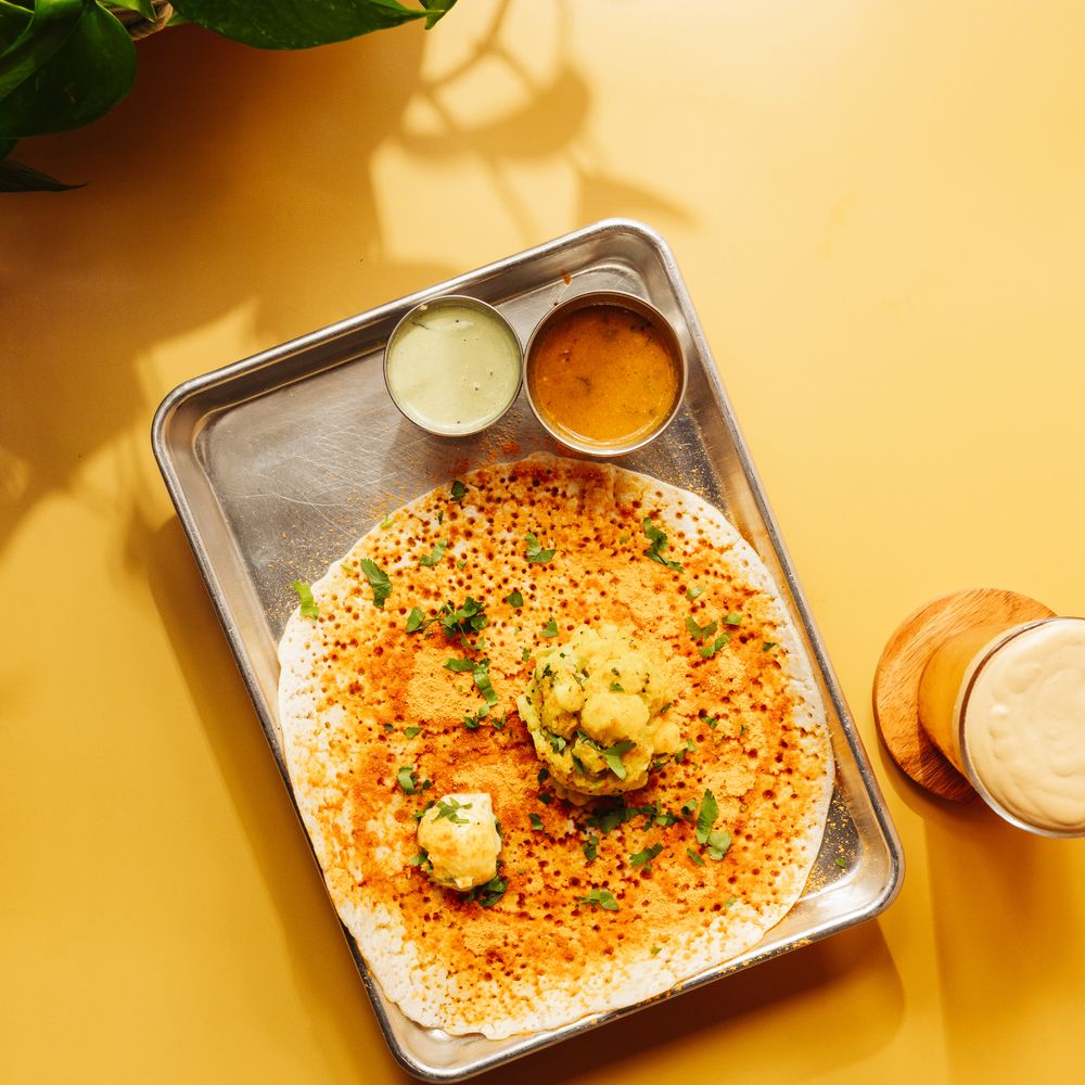 An open masala dosa on a steel tray with chutney and sambar