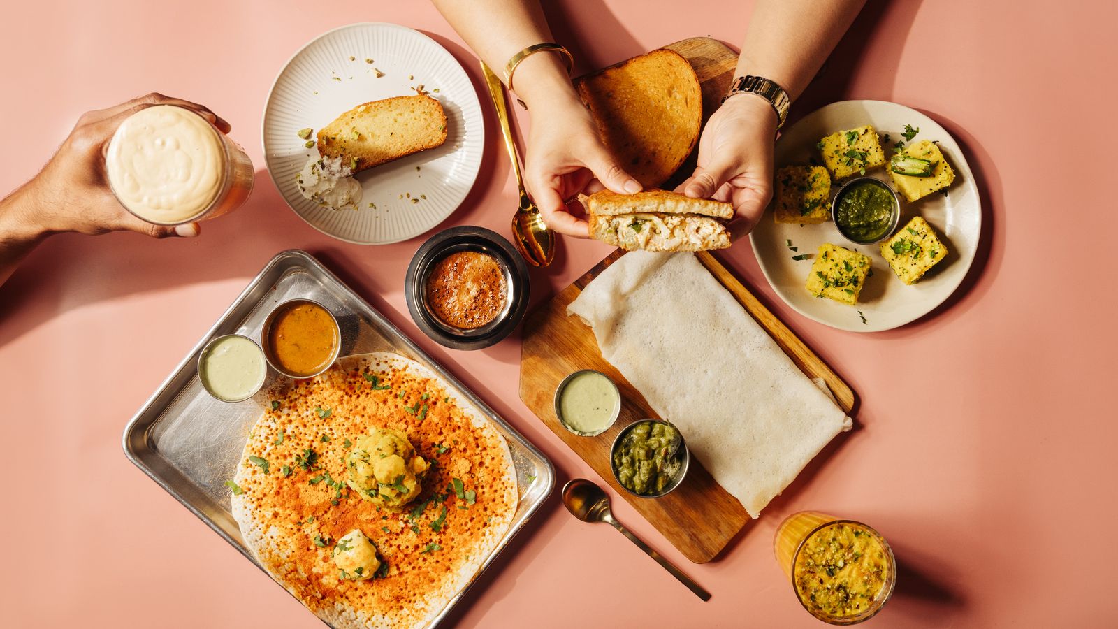 A table at Thindi Cafe seen from above, with hands reaching for a sandwich beside a filter coffee